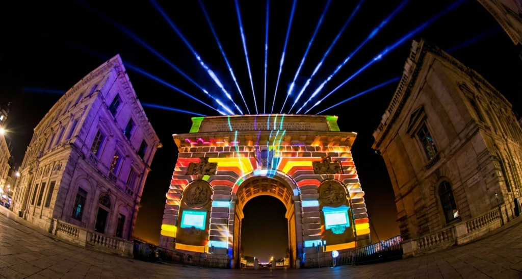 Spectacle de vidéo mapping monumental avec des projections géométriques colorées et des faisceaux laser sur la façade d'une arche historique pour un événement au Maroc.